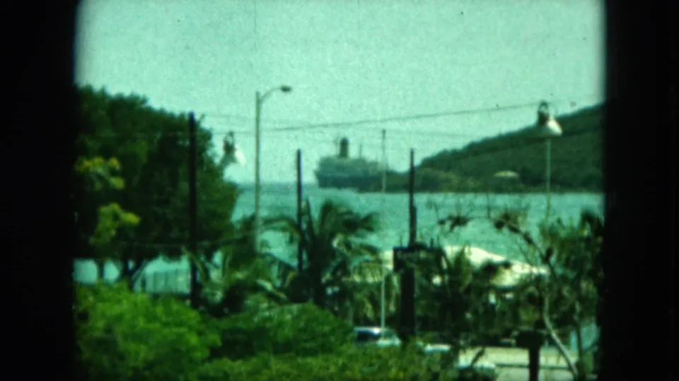 The final frame shows a ship offshore near a green hillside, with palms, streetlights, cars, and a dark window frame in the foreground.