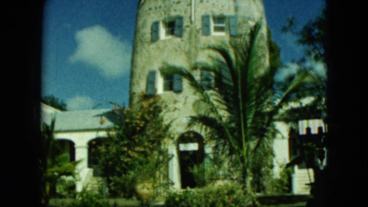 Stone building with arched doorway, shuttered windows, palm fronds, and blue sky.