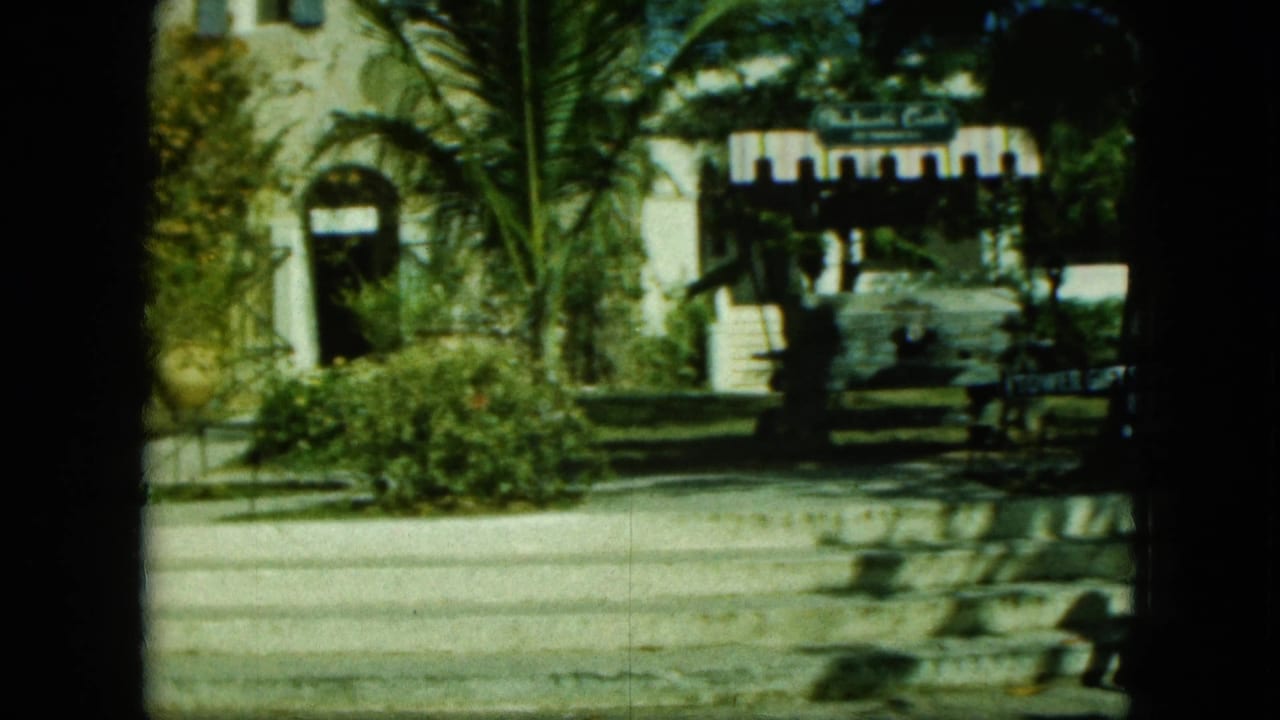 White arched building, palms, road, and Tower Gift Shop sign seen across a sunlit street.