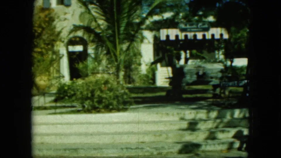 1960s 8mm travel frame showing a white arched building, palms, greenery, road, and a visible Tower Gift Shop sign.