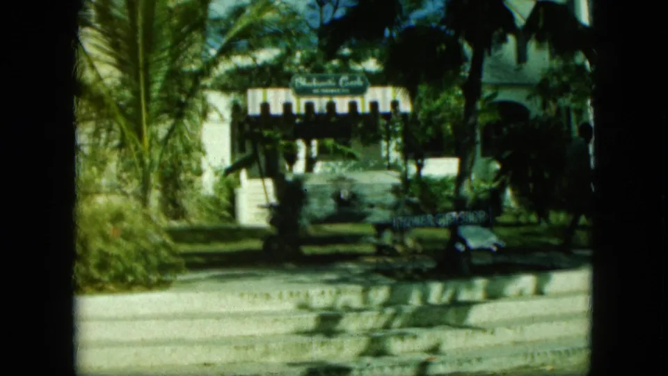 1964 home-movie frame in Saint Thomas showing palms, a tower-area sign, the Tower Gift Shop sign, a sidewalk, and a parked car.