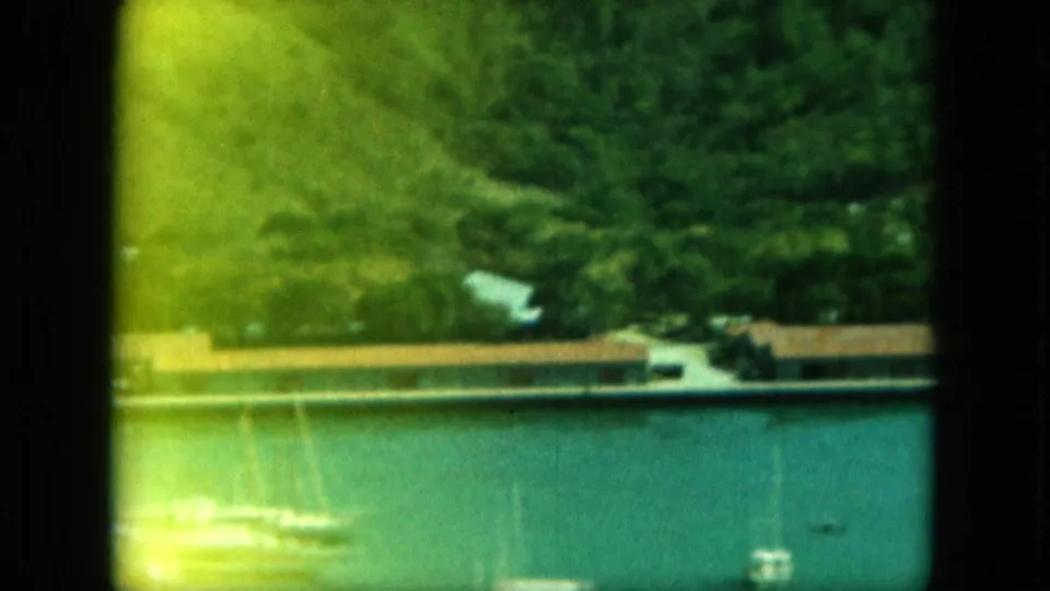 Soft green-tinted 8mm frame of Saint Thomas waterfront buildings beside harbor water, with small boats and dense hillside above.
