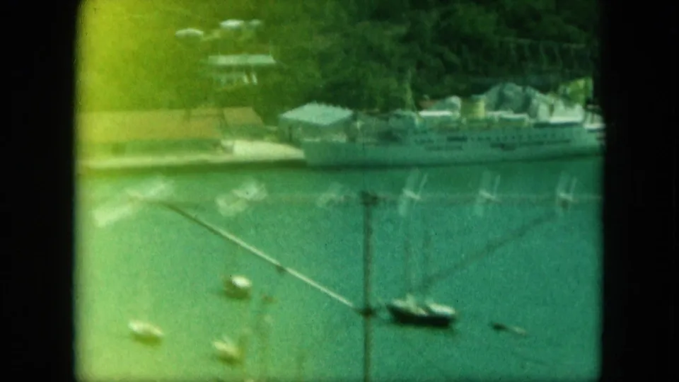 Cataloged 1964 Saint Thomas harbor view with a large white ship at the dock, small boats, piers, shoreline structures, and green hillside.