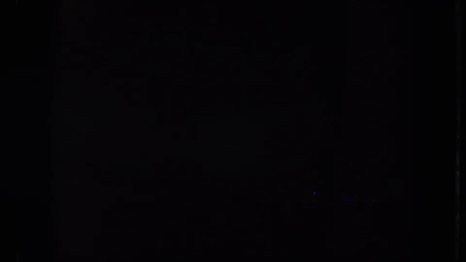 Mostly black 8mm frame area with faint blue light marks and visible film border, likely the end or gap of the brief clip.