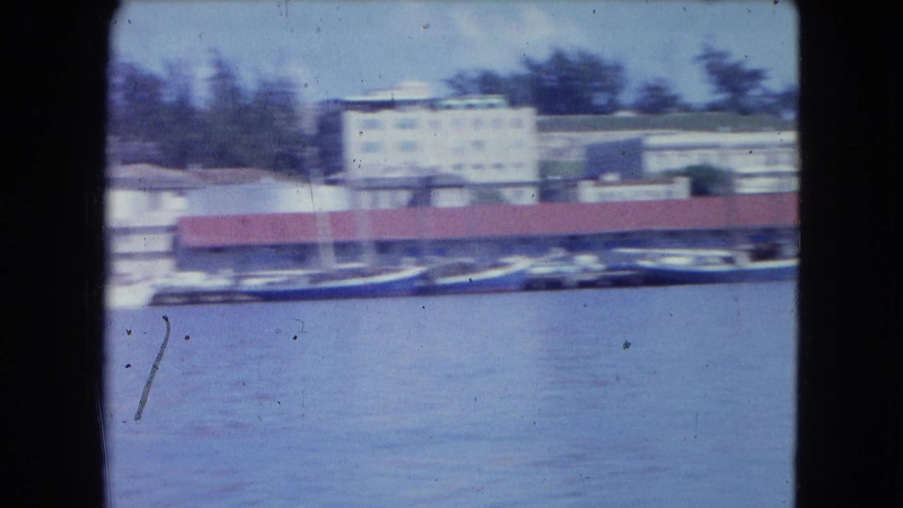 Blurred harbor shoreline with boats, red-roof buildings, and pale industrial structures.