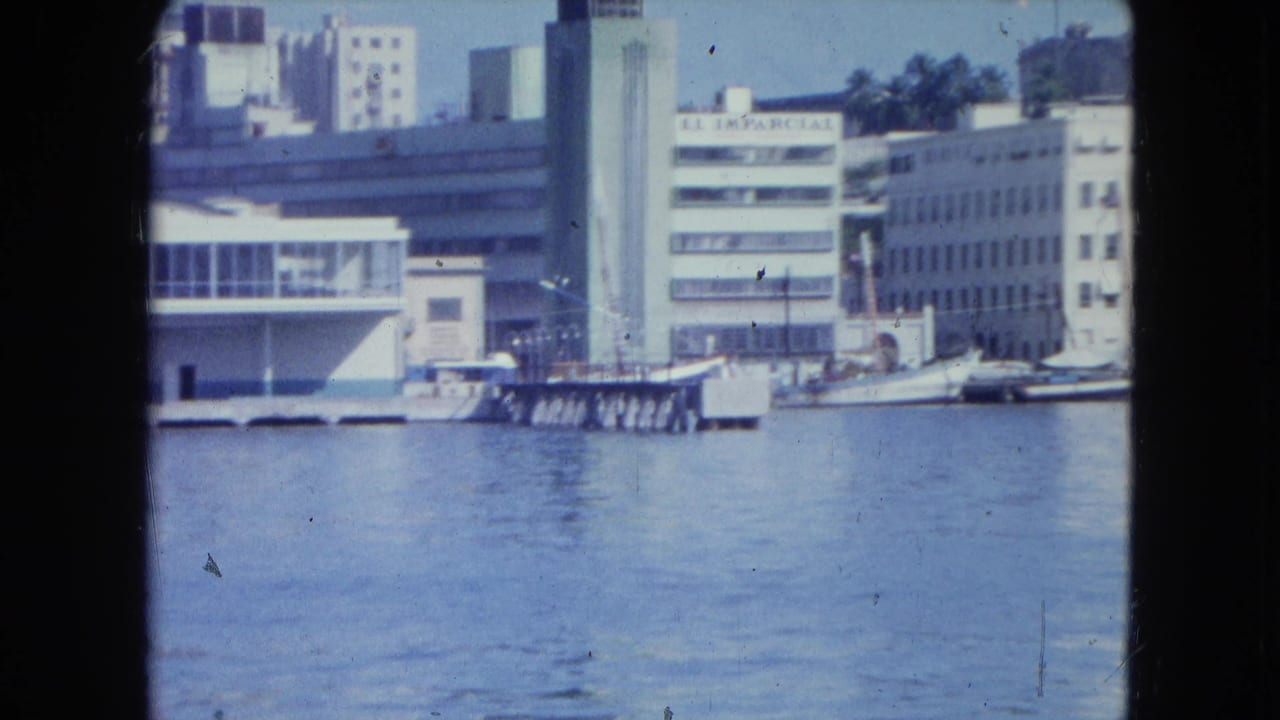 1964 San Juan waterfront viewed from a boat, with harbor water, piers, white buildings and a dark vertical foreground divider.
