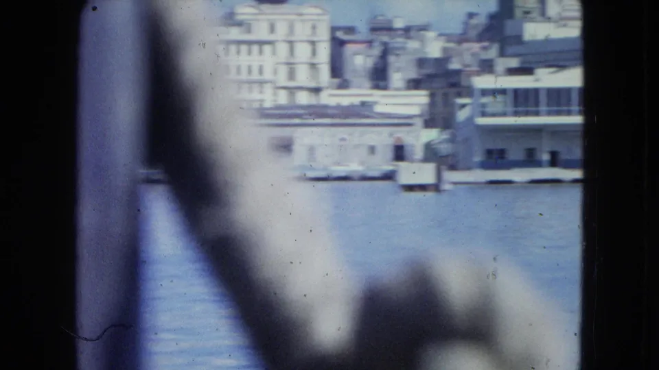 1964 San Juan shoreline appears partially blurred from a moving boat, with water, buildings and dark foreground obstructions.