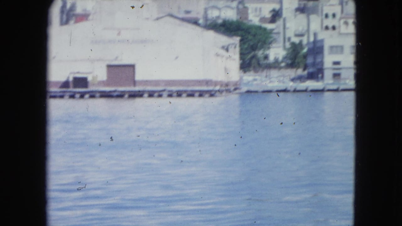 San Juan inner harbor view from 1964 footage, with calm water and pale waterfront buildings in soft focus.
