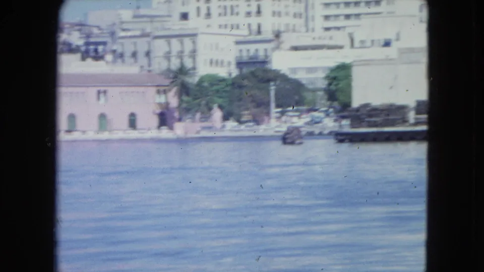 San Juan inner harbor view from 1964, with waterfront facades, trees, a dock area, and calm blue water.