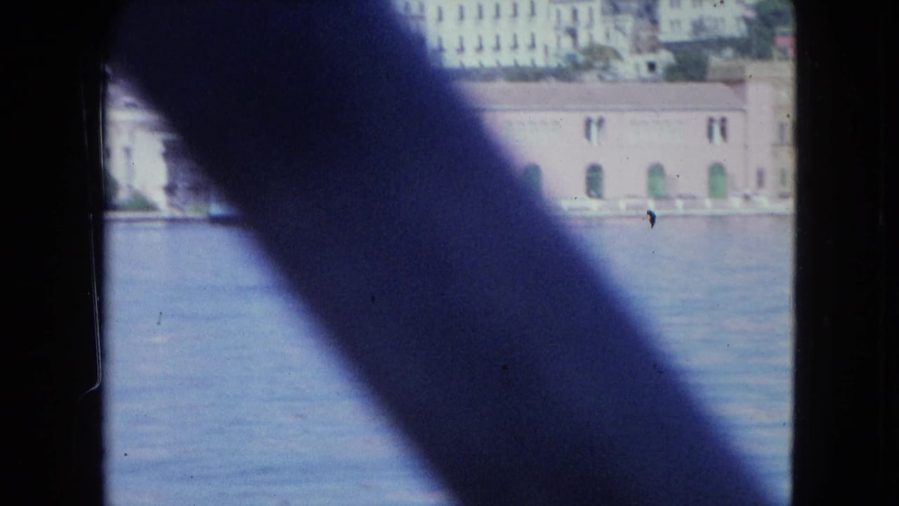 Boat-window frame crosses a harbor view of waterfront buildings and water.