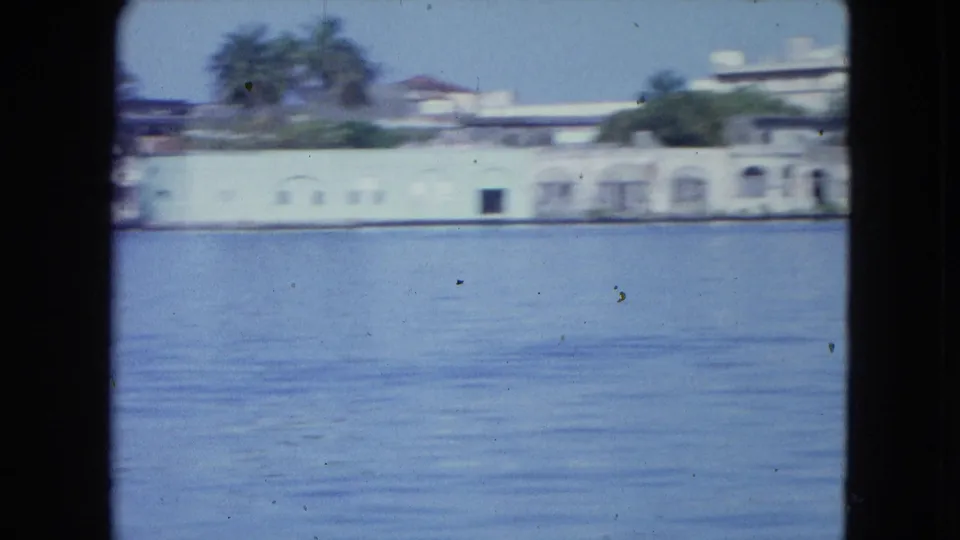 San Juan harbor view with a long white waterfront structure, arched openings, green doors or shutters, palms, and calm blue water.