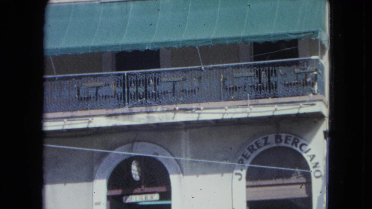1964 San Juan building exterior with green awning, ornate balcony railing, and partial arched signage above a storefront.