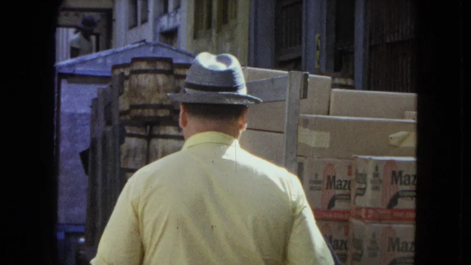 San Juan street footage showing a fedora-wearing man from behind beside stacked boxes and containers outside a building.