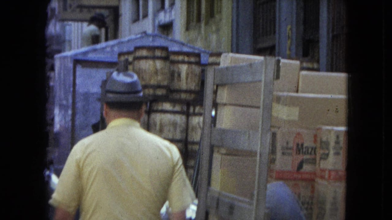 Rear view of a man in a yellow shirt moving through a San Juan street beside Mazza-marked cartons and a delivery vehicle.