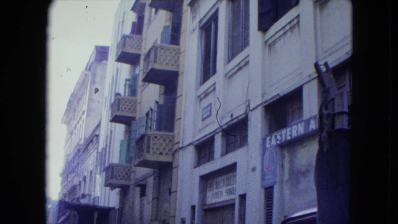 Narrow street view with multistory buildings, latticed balconies, and a faded sign.