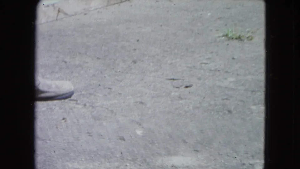 A light shoe passes near a small lizard-like animal on pavement in this 1964 San Juan home-movie frame.