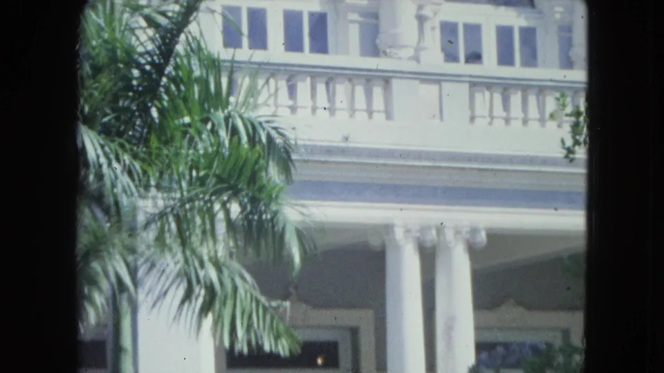 A white house with columns, balcony railing, windows, and palm fronds appears in the 1964 San Juan home-movie footage.