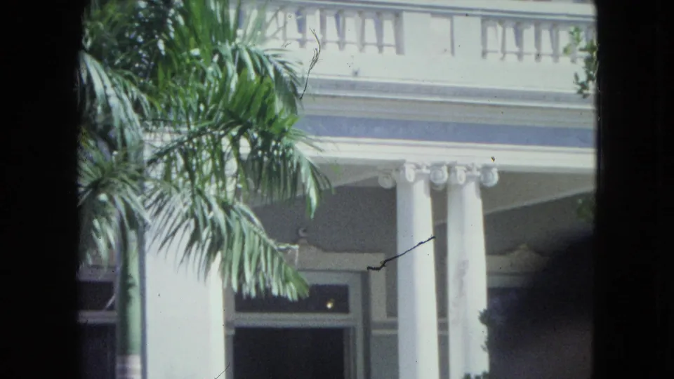 Palm fronds partially cover a white columned house exterior in San Juan, captured on 8mm film in 1964.