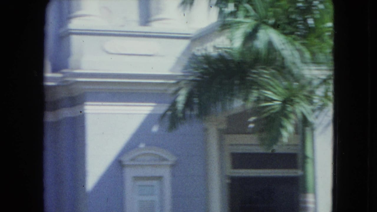 1964 San Juan exterior view showing a pale colonial-style facade, palm fronds, and a dark window or doorway opening.