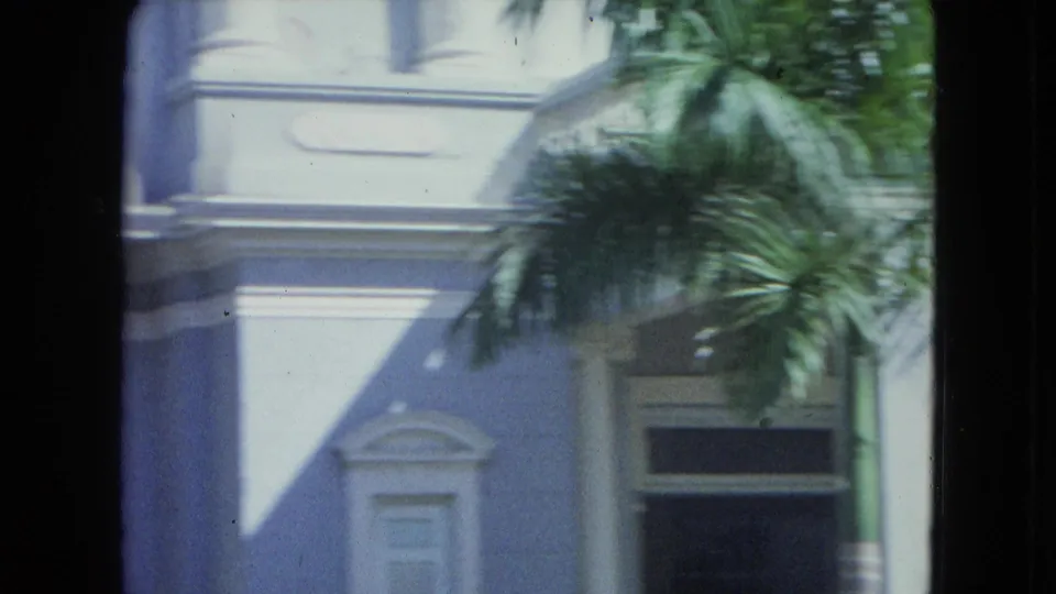 1964 San Juan exterior view showing a pale colonial-style facade, palm fronds, and a dark window or doorway opening.