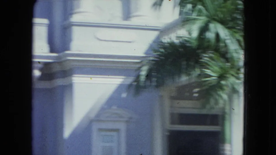 1964 San Juan exterior detail with palm fronds, angled shadow, dark window opening, and colonial-style trim on the facade.