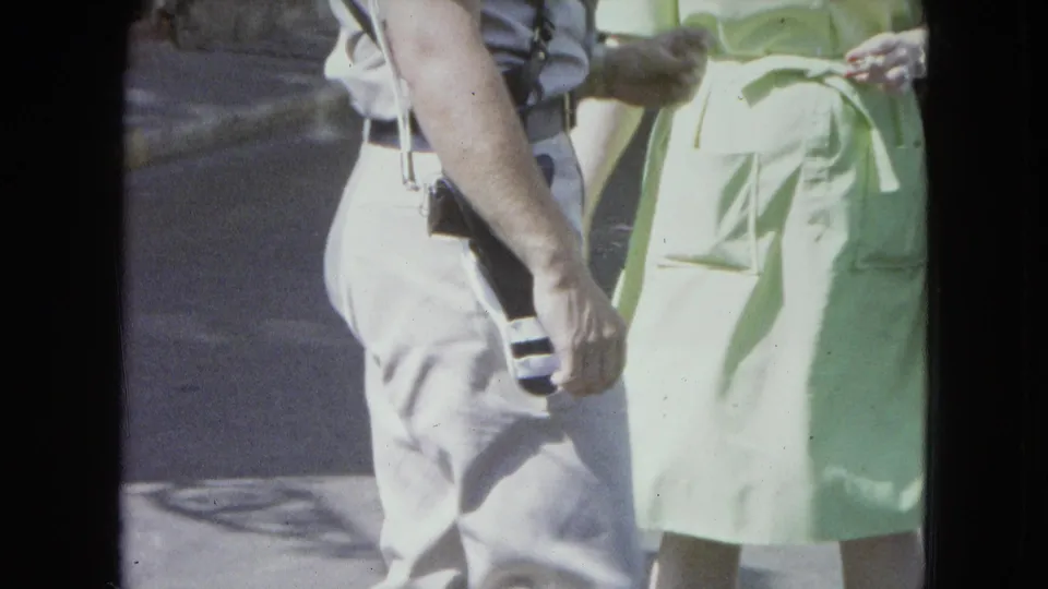 Close 1964 street-level home-movie view of adults walking, with light summer clothing and a handheld camera angle.