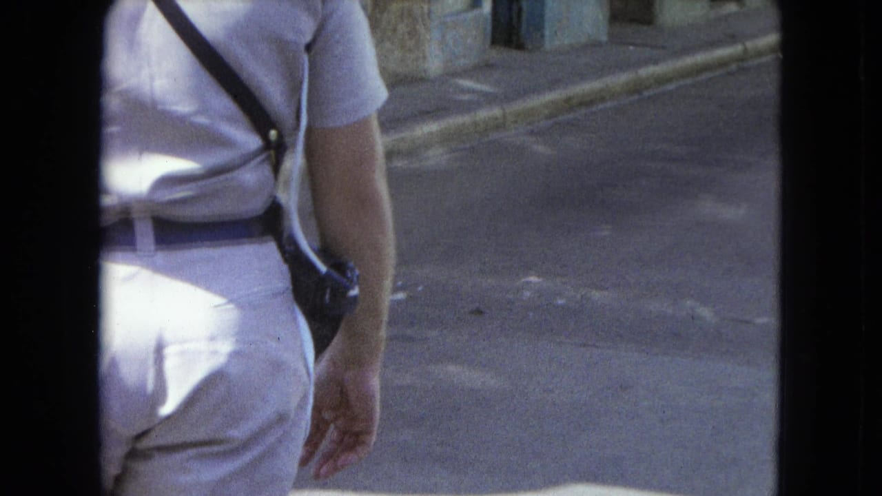 Light-uniformed man with belt, shoulder strap, and side-mounted radio walking along a San Juan street in 1964 footage.