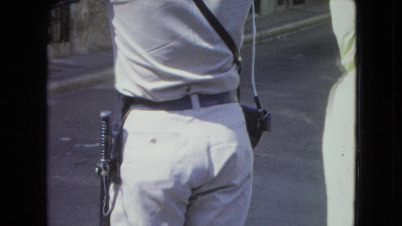 Uniformed police officer seen from behind walking beside a woman in a pale green dress.