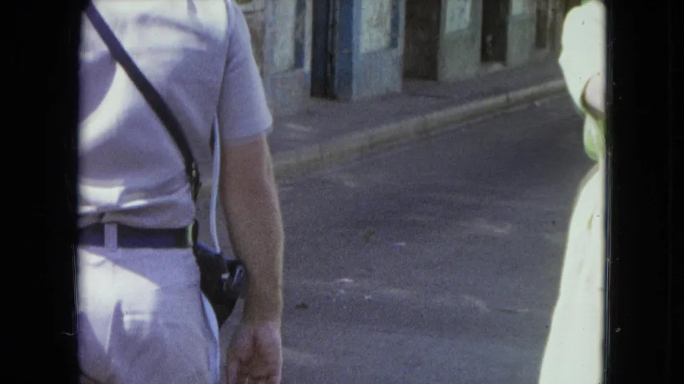 1964 San Juan frame with a man seen from behind and a woman partly cropped at the edge of a street.