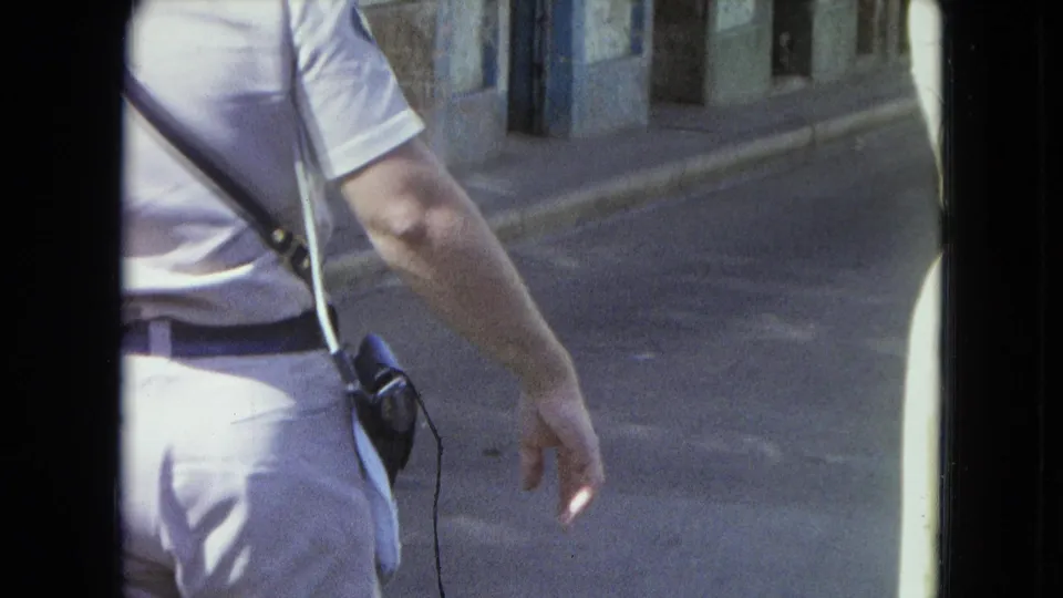 1964 San Juan home-movie frame of a man in light clothing walking near a woman at the edge of the shot.