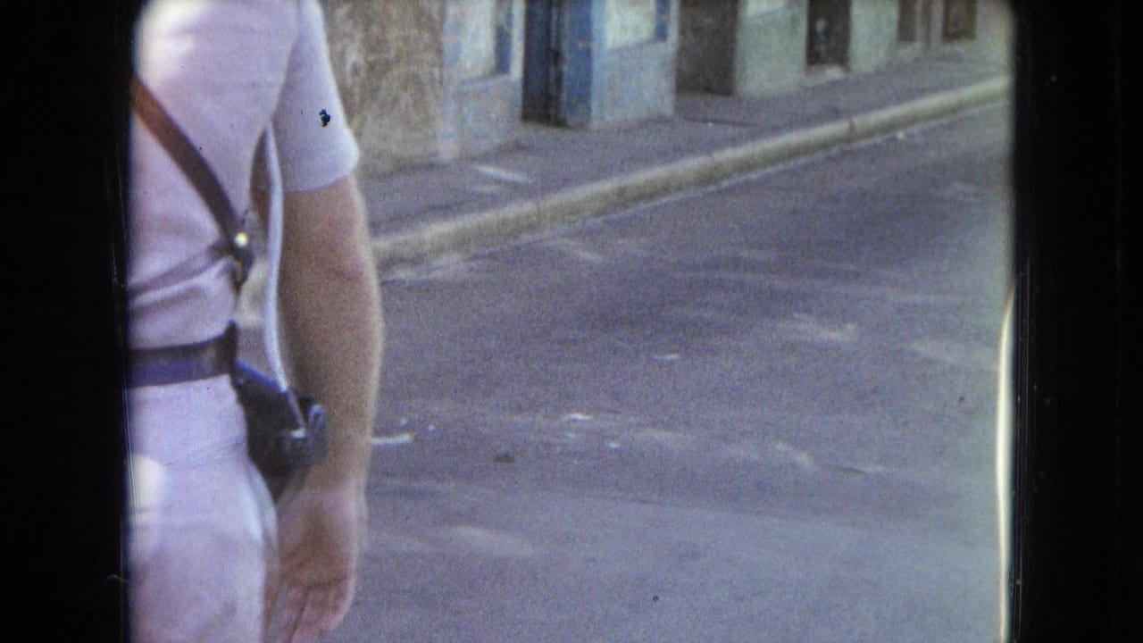 1964 San Juan home-movie frame showing a partial adult figure walking past a quiet street with aged building fronts.