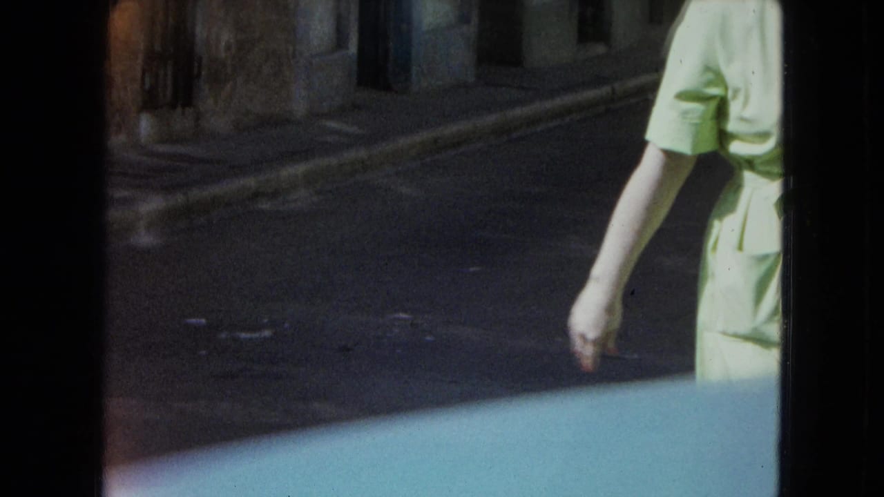 1964 San Juan frame with a partial walking figure near a narrow street and weathered masonry building exterior.