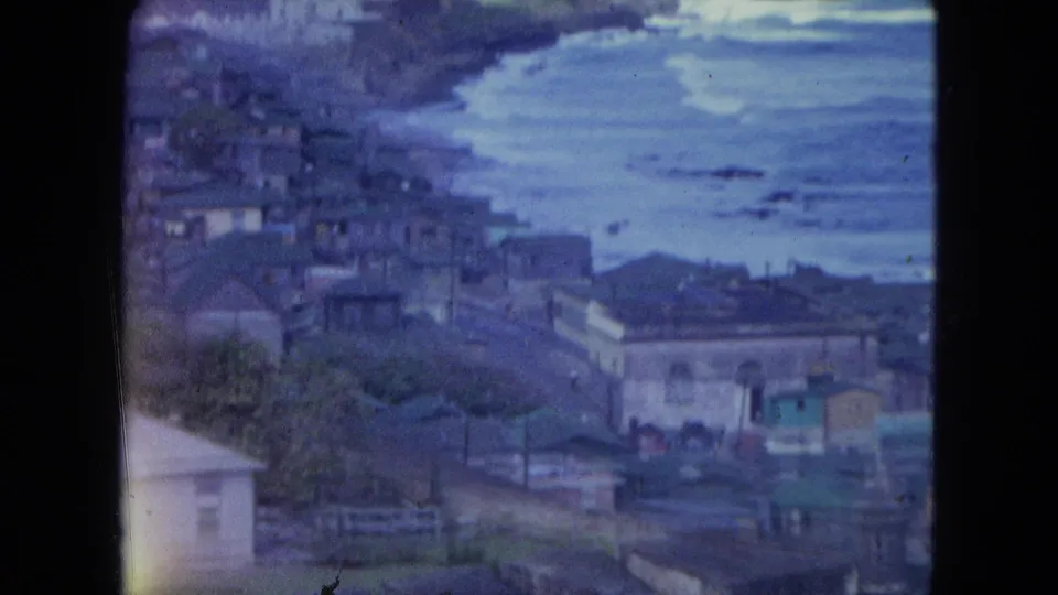 Elevated 1964 view over San Juan coastal buildings toward the water, with rooftops and shoreline visible through faded 8mm color.