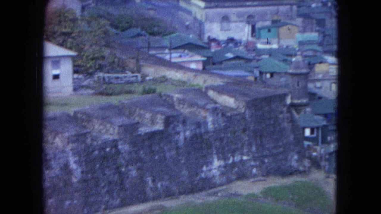 1964 San Juan footage showing dense coastal buildings, green roofs, and stone walls above a rocky shore.
