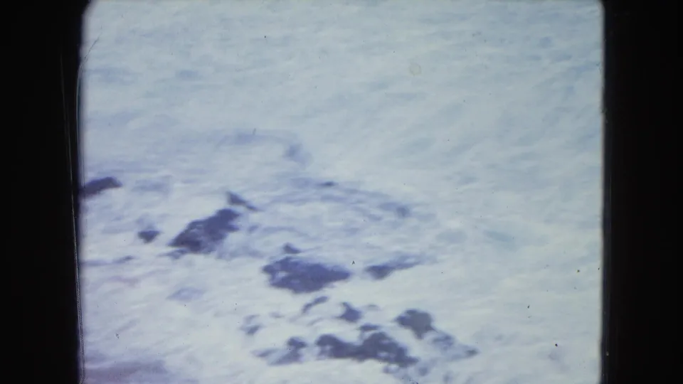 1964 San Juan beach footage showing foamy ocean water spreading around dark rocks near the shore.
