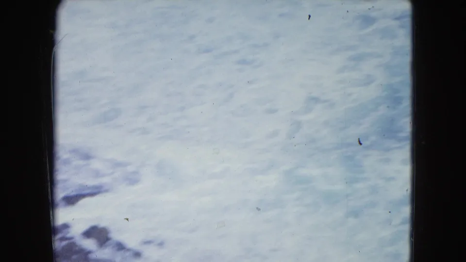 1964 San Juan shoreline footage shows pale blue water and white foam seen close up through visible 8mm gate edges.