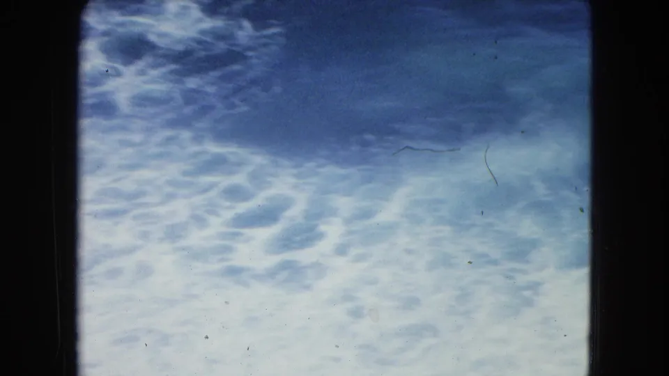 The frame shows turbulent blue water and white foam near shore in the 1964 San Juan home-movie clip.