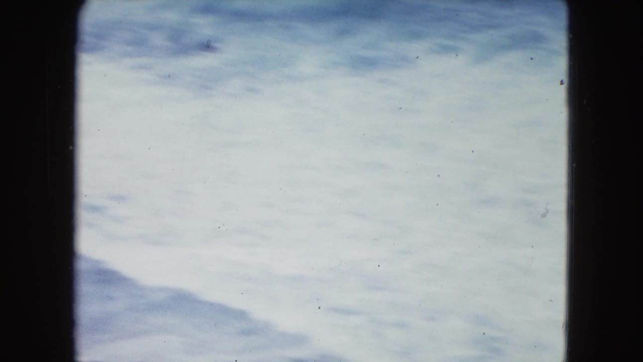 Pale surf and a distant shoreline shape framed by dark film borders.