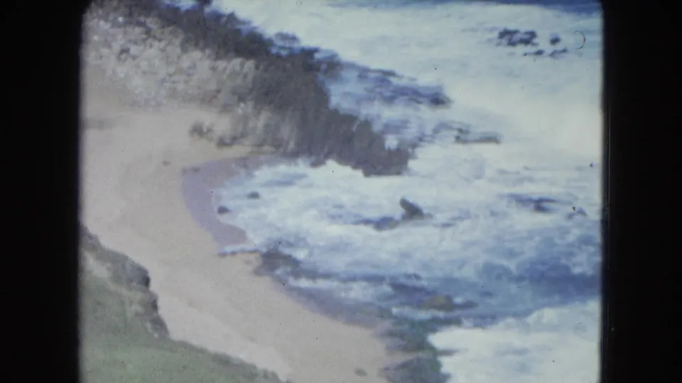 The final 8mm frame shows white surf, pale sand, and a rocky shoreline on a San Juan, Puerto Rico beach in 1964.