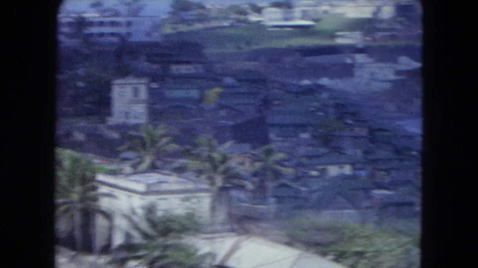 Elevated 1964 San Juan view with palm trees, rooftops, hillside buildings, and soft blue 8mm color shift.