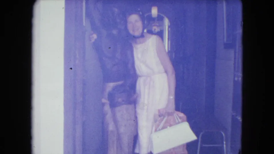 A woman in a light dress poses inside a dim corridor beside a sculptural figure, with handbags visible near her feet.