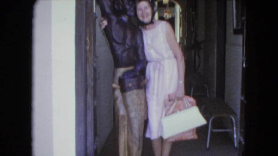 A slightly blurred 8mm frame shows the woman standing close to the statue in the narrow San Juan interior.