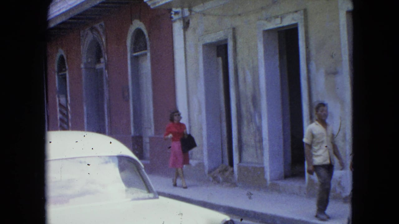 1964 San Juan street view with colonial-style facades, a white car hood, and pedestrians moving along the sidewalk.