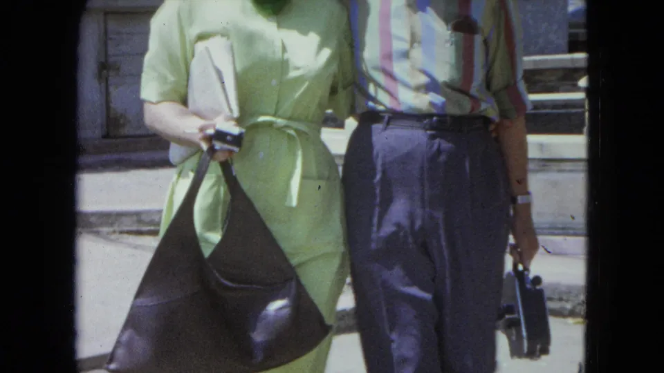 A close 8mm frame shows the couple's 1960s clothing, bags, and relaxed posture outside in San Juan, Puerto Rico.