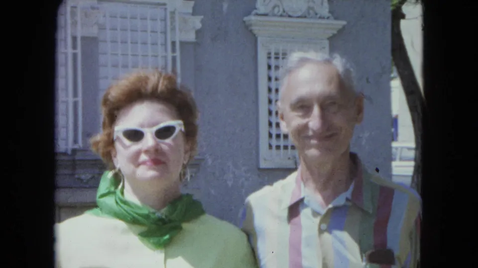 The woman in green and the man in a striped shirt face the camera outdoors in San Juan, Puerto Rico, in 1964 home-movie footage.