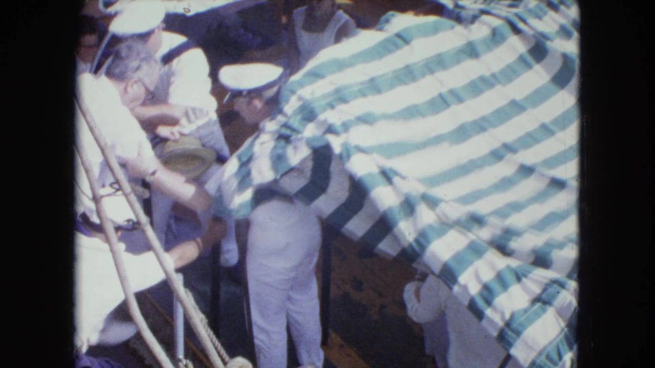 Sailors assist a man near a striped canopy on a small boat.