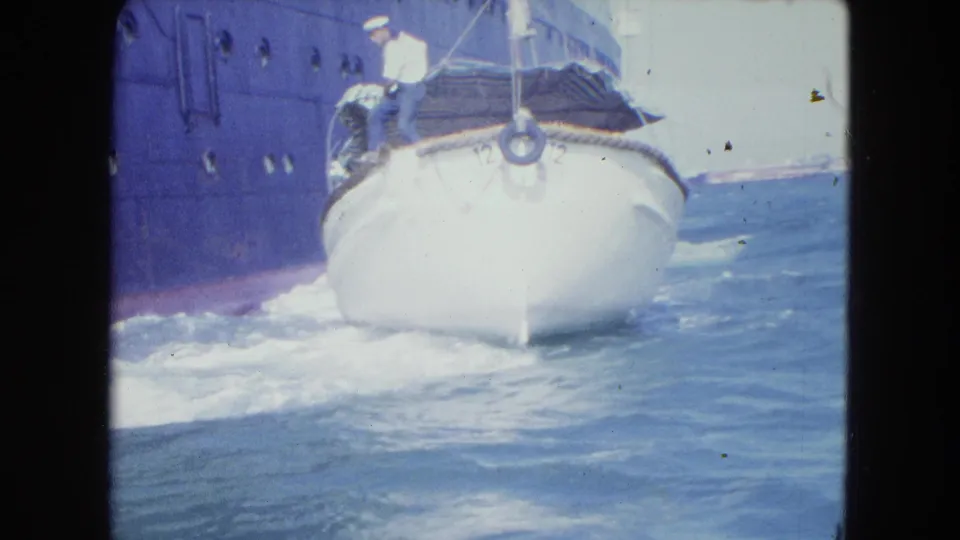 The small white boat travels through blue harbor water beside a large dark-hulled ship in San Juan.