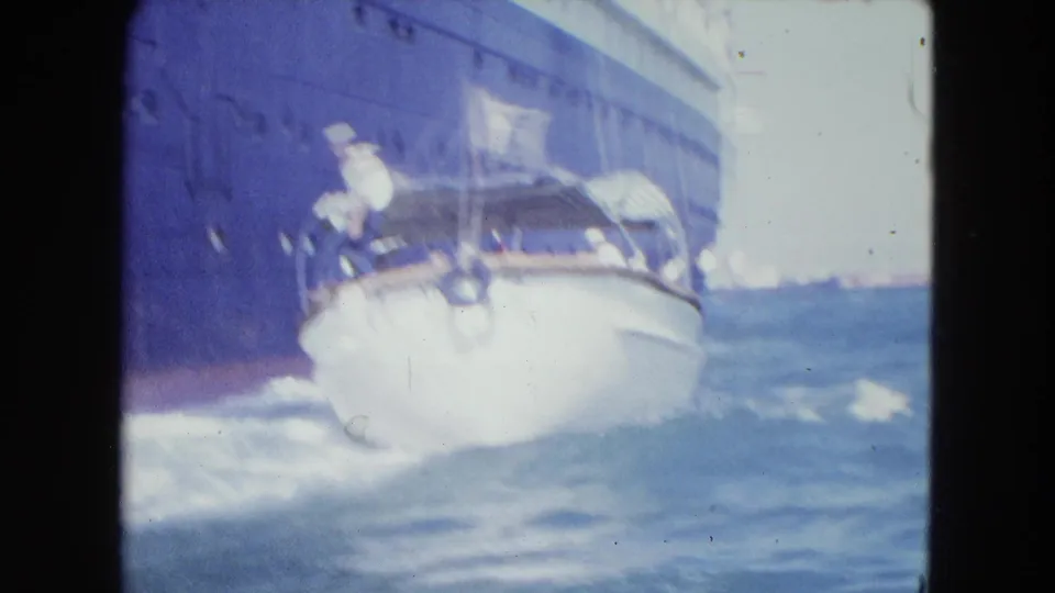 A small white launch moves through choppy San Juan harbor water beside a larger vessel, with a person visible on board.