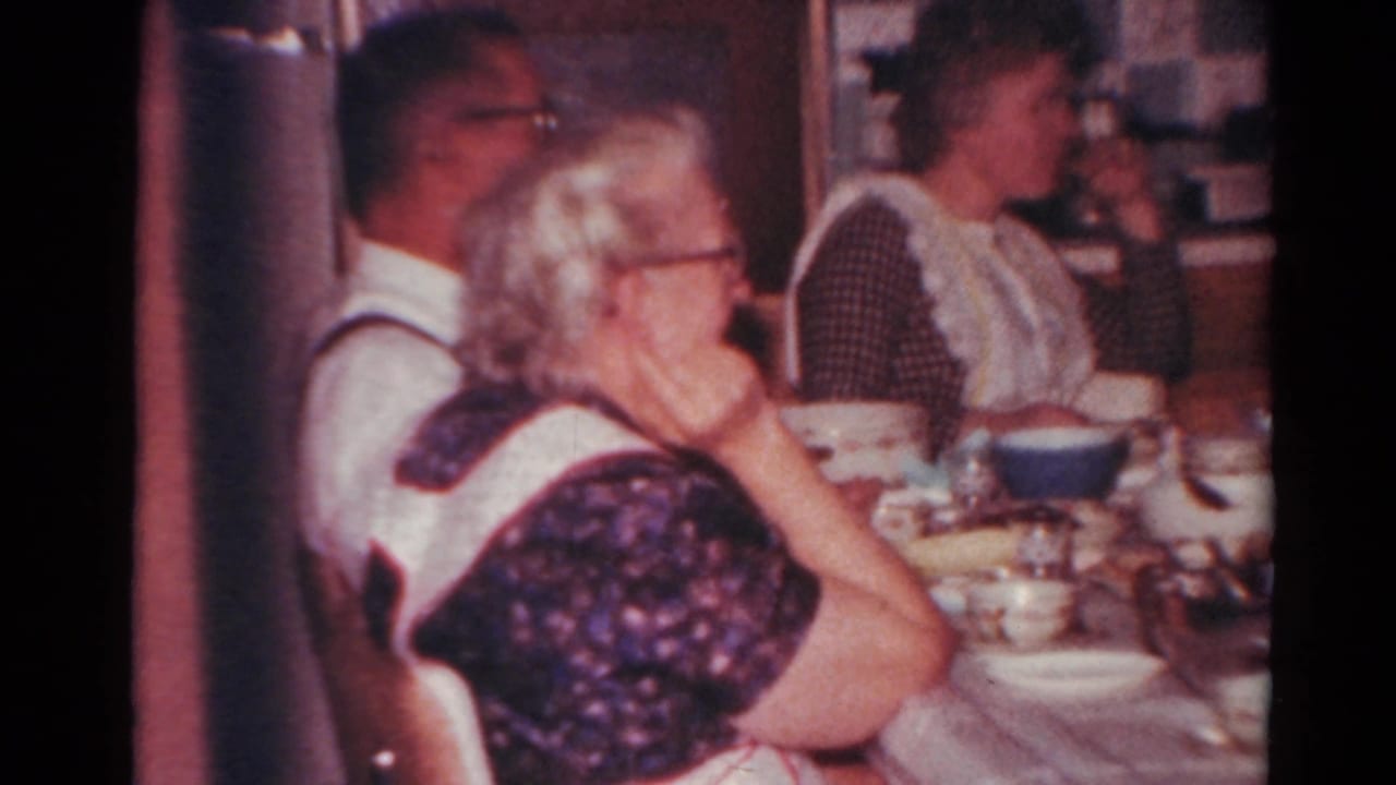 Adults at a kitchen table with bowls, cups, and dishes visible.