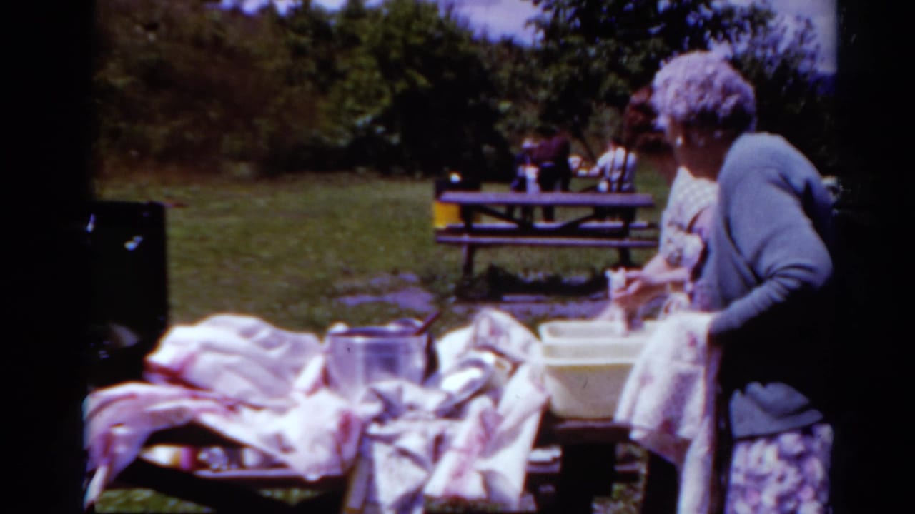 Two women, one with short gray hair and a blue cardigan, stand near picnic dishes and a yellow basin in Toledo, Ohio.
